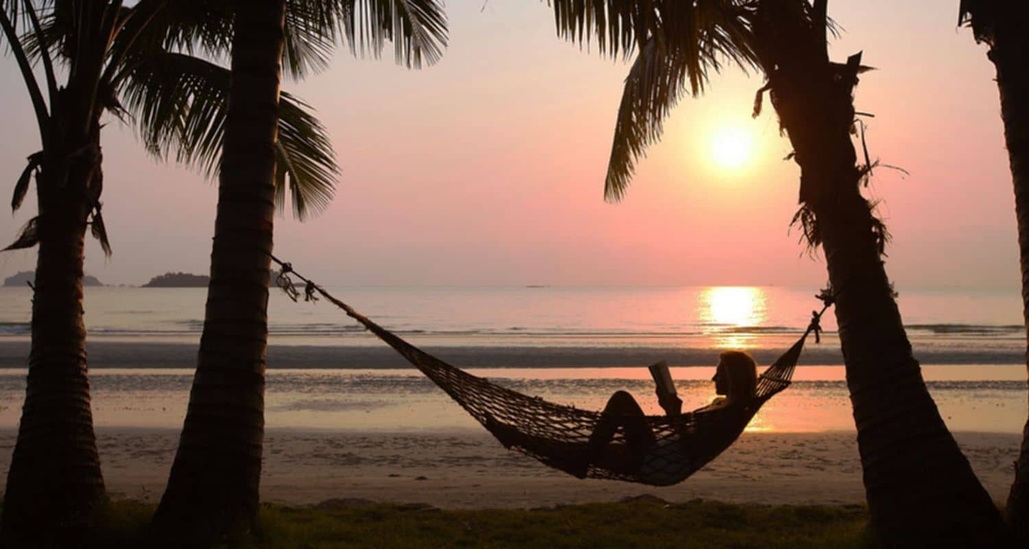 A woman reading a book by the sea at sunset