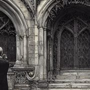 A man stands at the elaborate gothic door of a castle