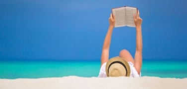 A woman reads a book on a beach