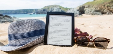 EReader on summer beach with sunglasses and summer hat